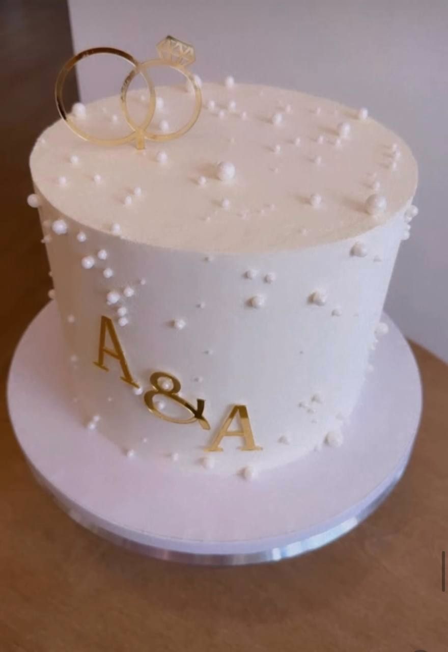 White cake with pearl dots, gold rings and A&A initials